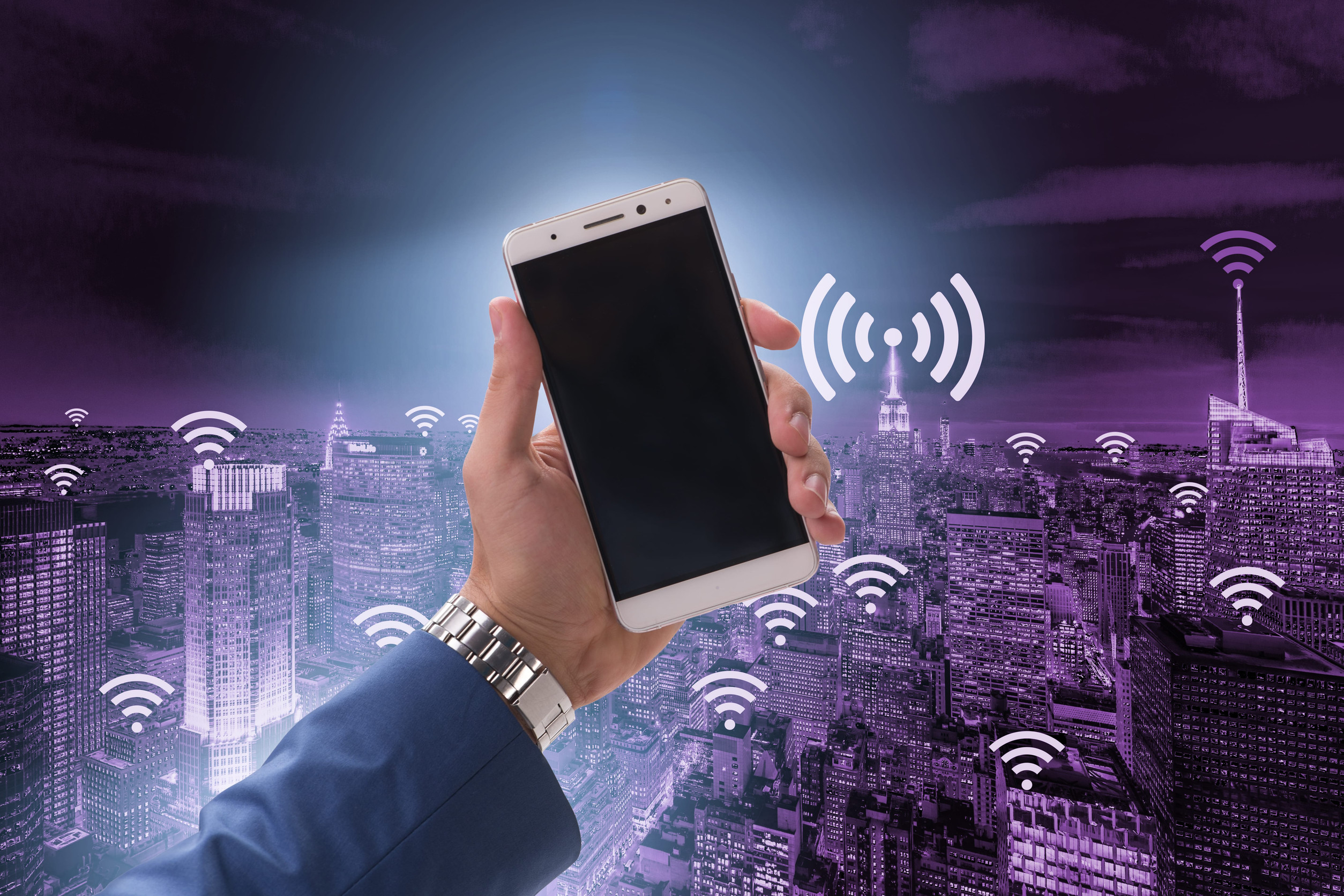 Hand Holding A Smartphone Against A City Skyline With Wireless Connectivity Network Symbols