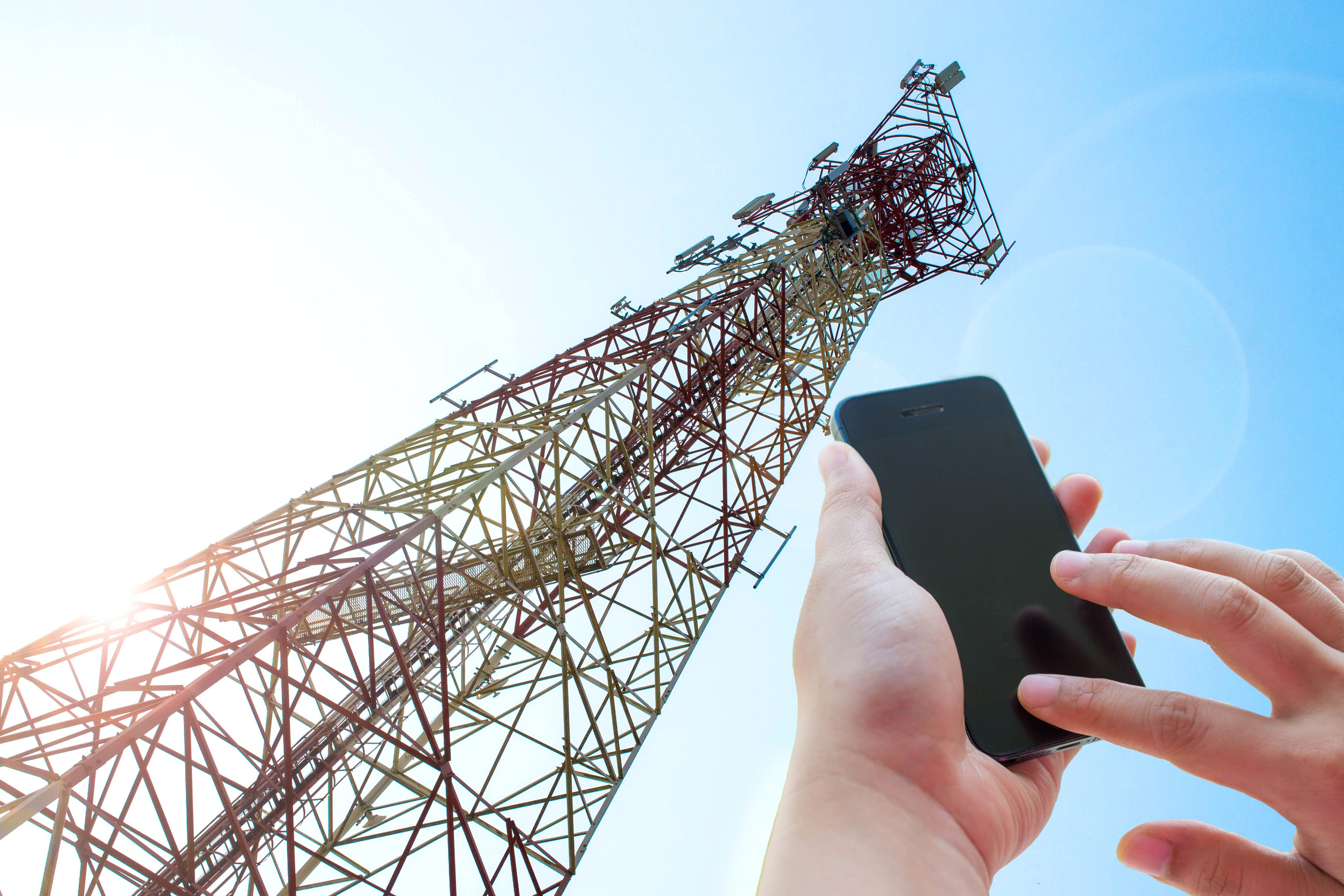 Person Using A Smartphone With A Cellular Telecommunications Tower In The Background