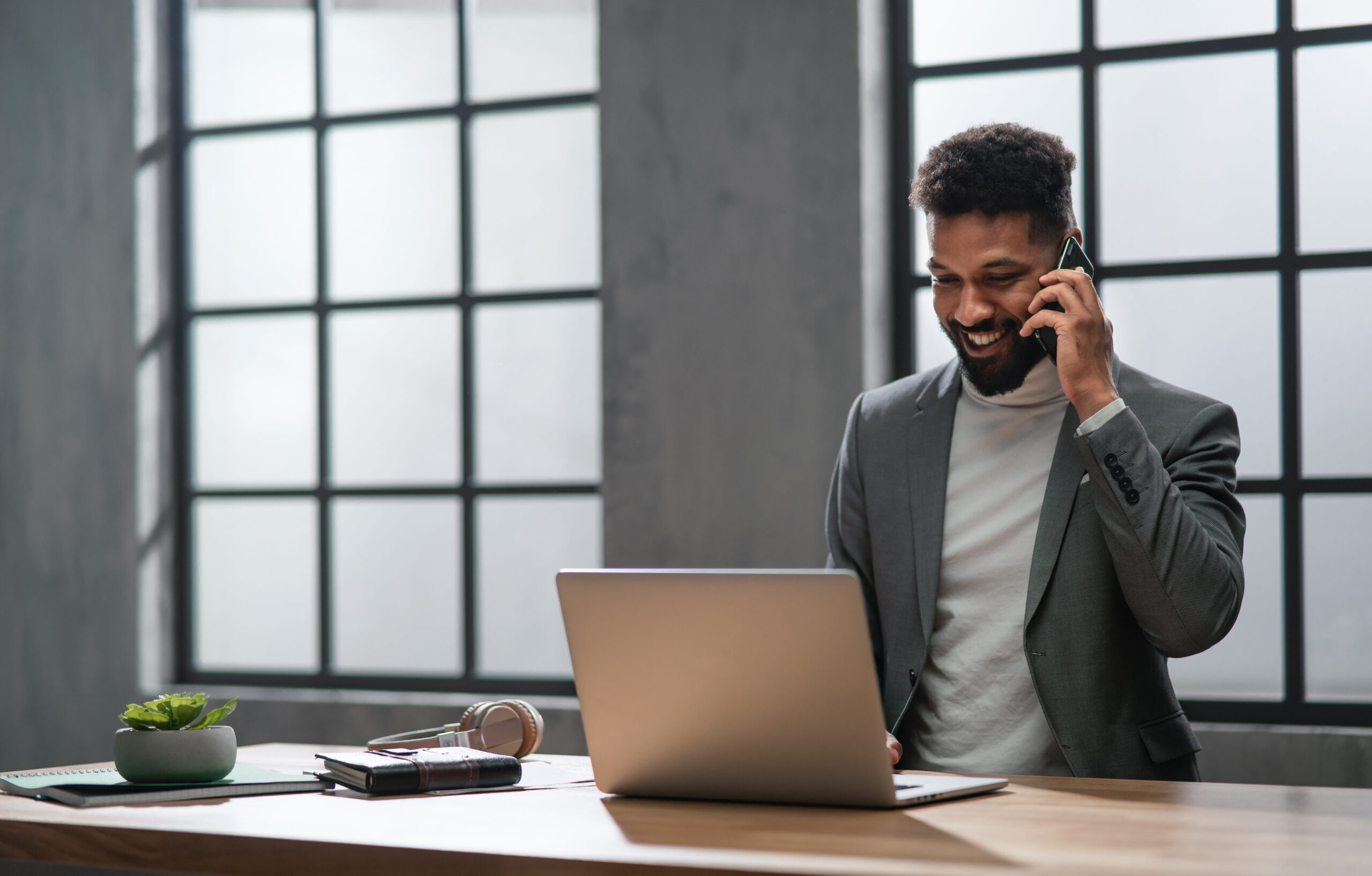 Businessman Talking On A Mobile Phone While Using A Laptop At His Office Desk